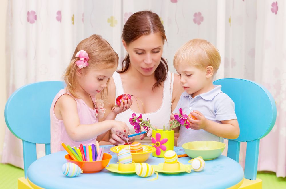 Young children painting holiday Easter eggs with their mom