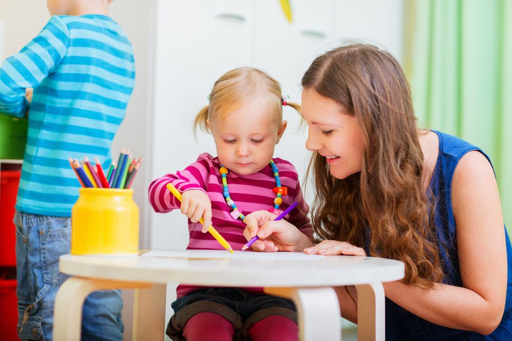 Toddler drawing a picture with her teacher at preschool