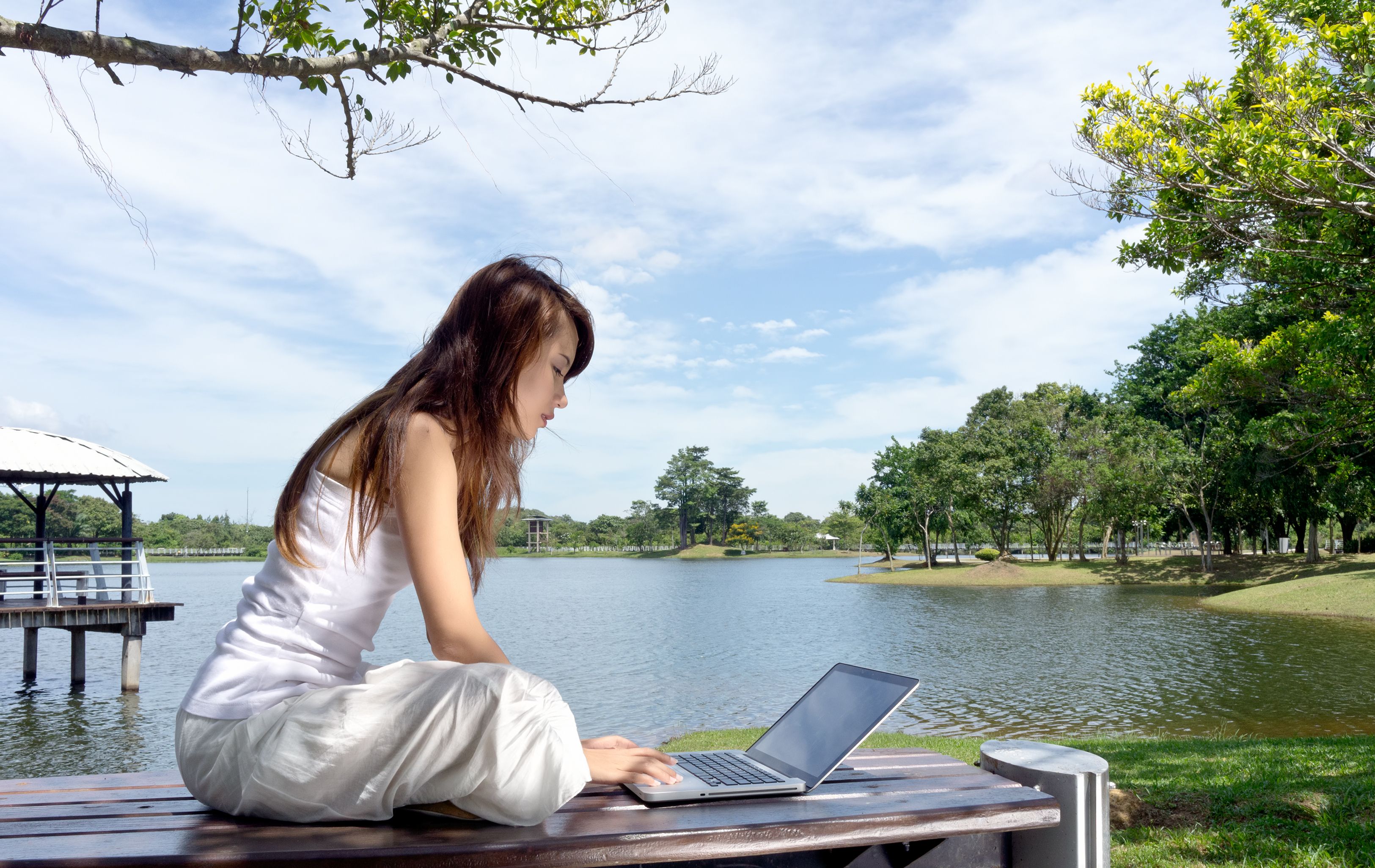 Young woman taking online classes with her laptop while relaxing at the beach of the lake