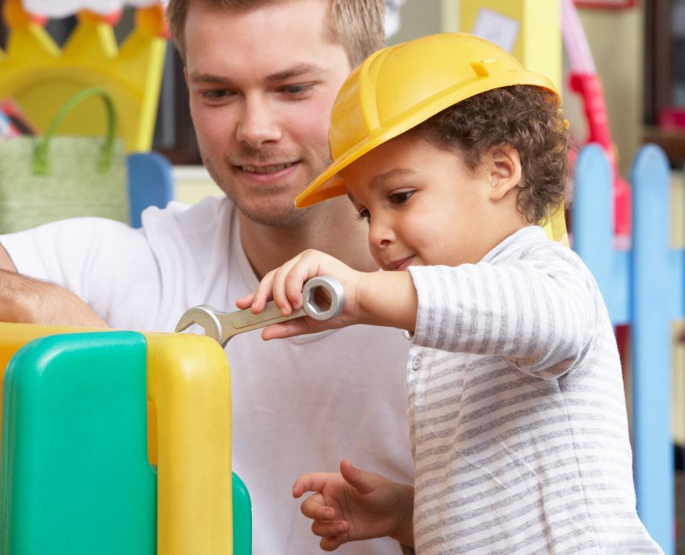 Male teacher showing young child how to use tools in preschool